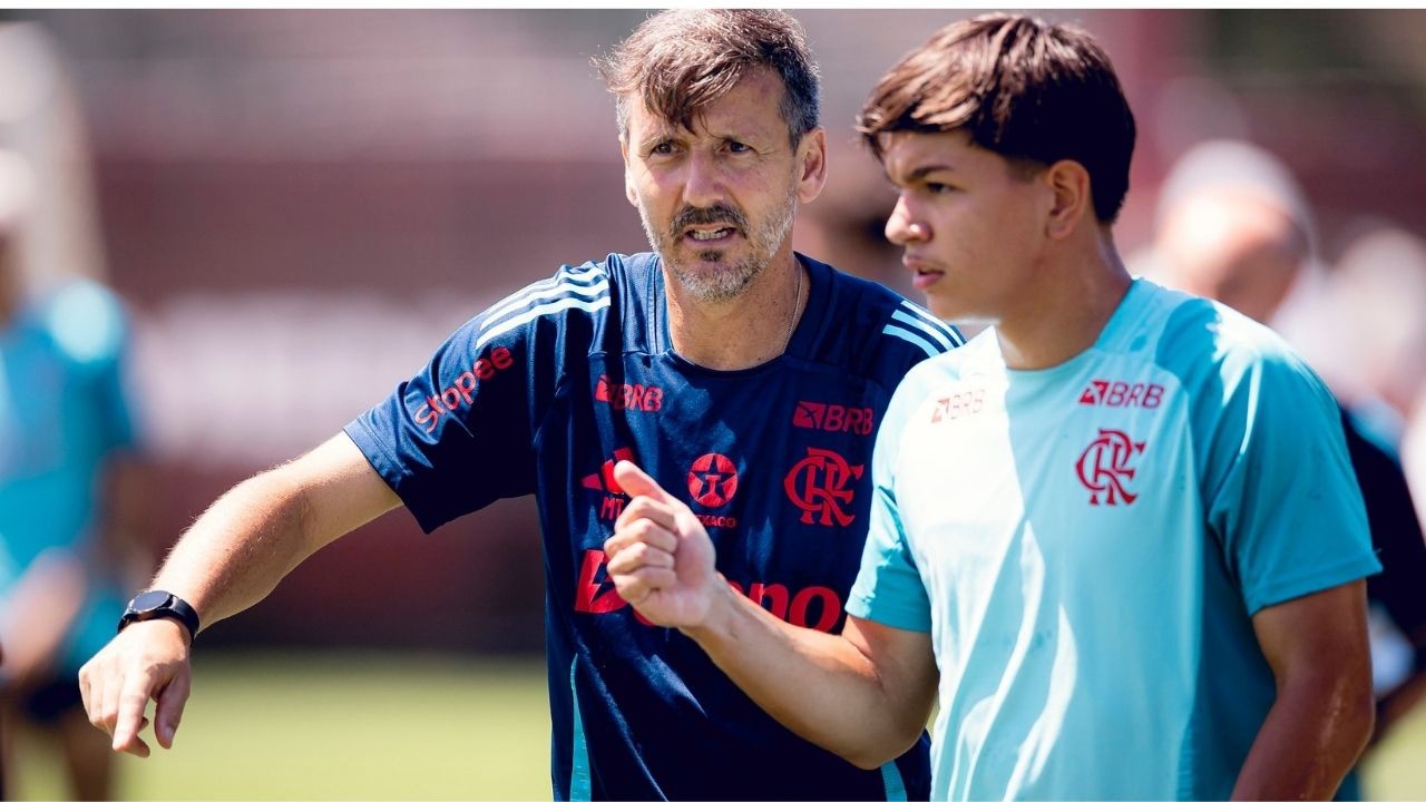 Treinador do Flamengo de camisa azul conversa com jovem jogador de camisa clara em campo.