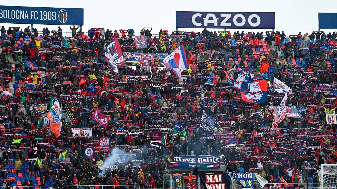 Multidão de torcedores do Bologna no estádio, com bandeiras e cachecóis vermelhos e azuis.