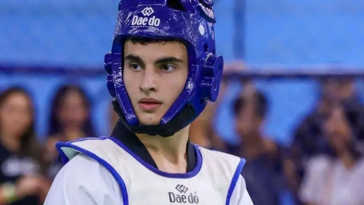 Jovem atleta Cauã Batista de taekwondo com capacete azul e protetor branco.