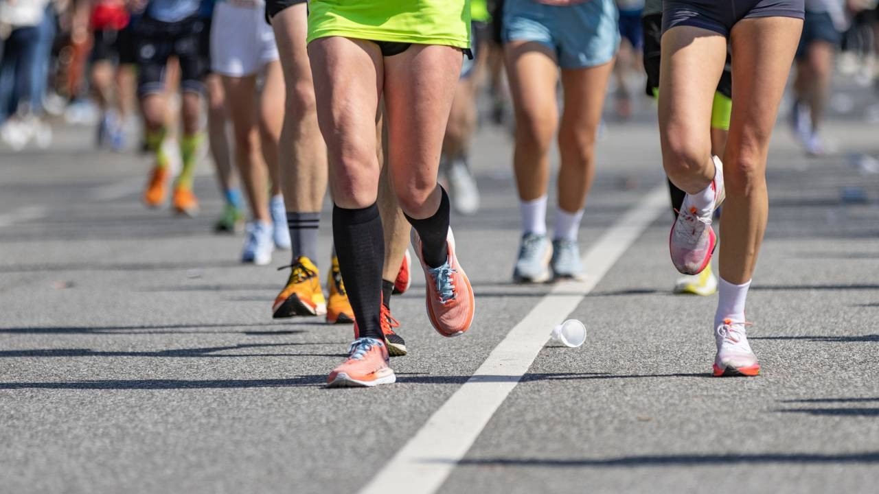 Pernas de corredores em movimento durante uma maratona, com tênis e um copo descartável no asfalto.