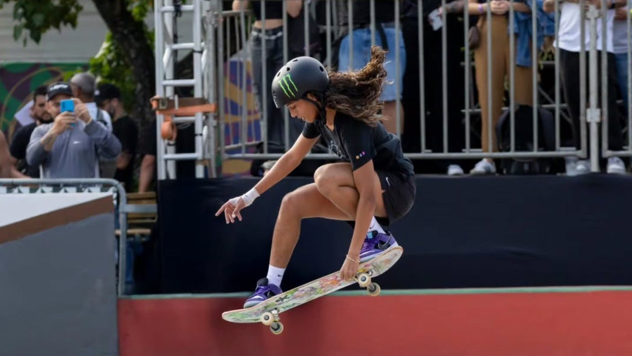 Jovem skatista feminina com capacete Monster Energy realizando manobra aérea em pista de skate.