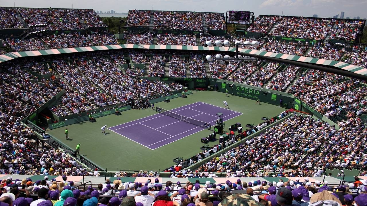 Vista panorâmica do estádio lotado do Miami Open, com quadra de tênis roxa e dois jogadores.