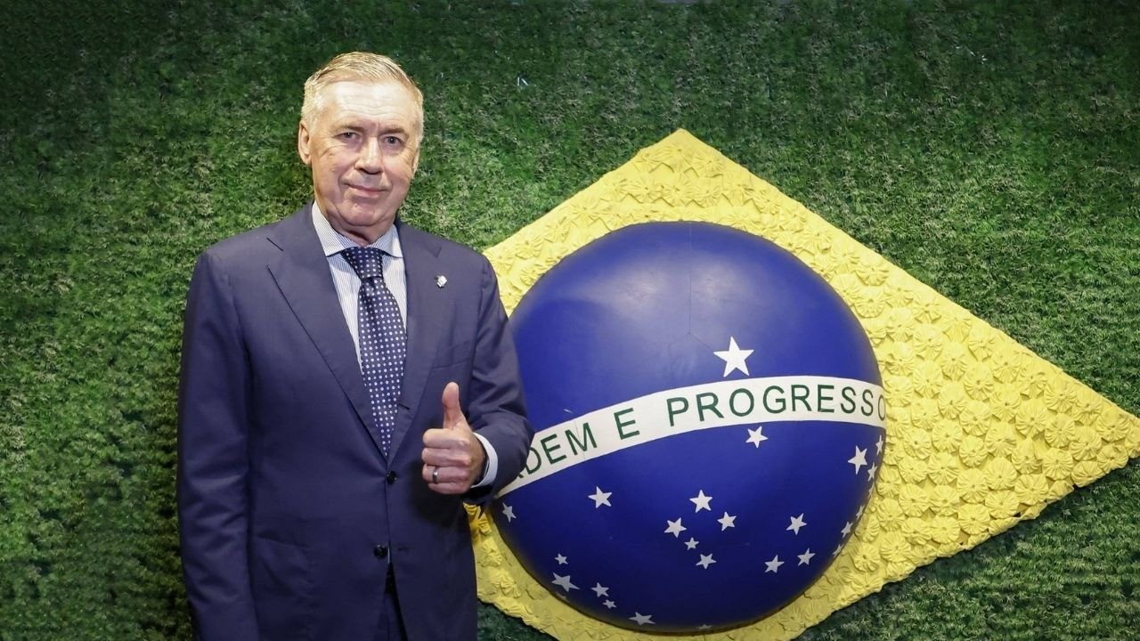 Carlo Ancelotti sorri, polegar para cima, ao lado do globo da bandeira brasileira.