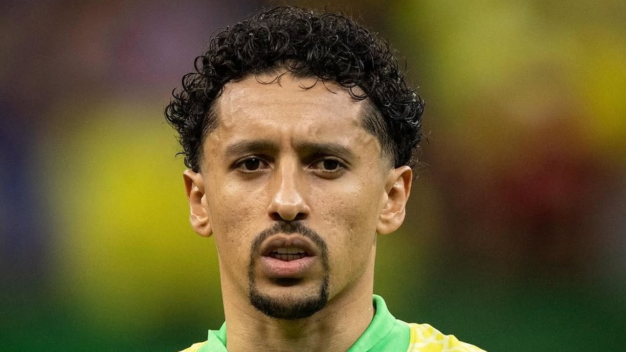 Marquinhos, jogador de futebol, com camisa verde e amarela, cabelo crespo e olhar sério.