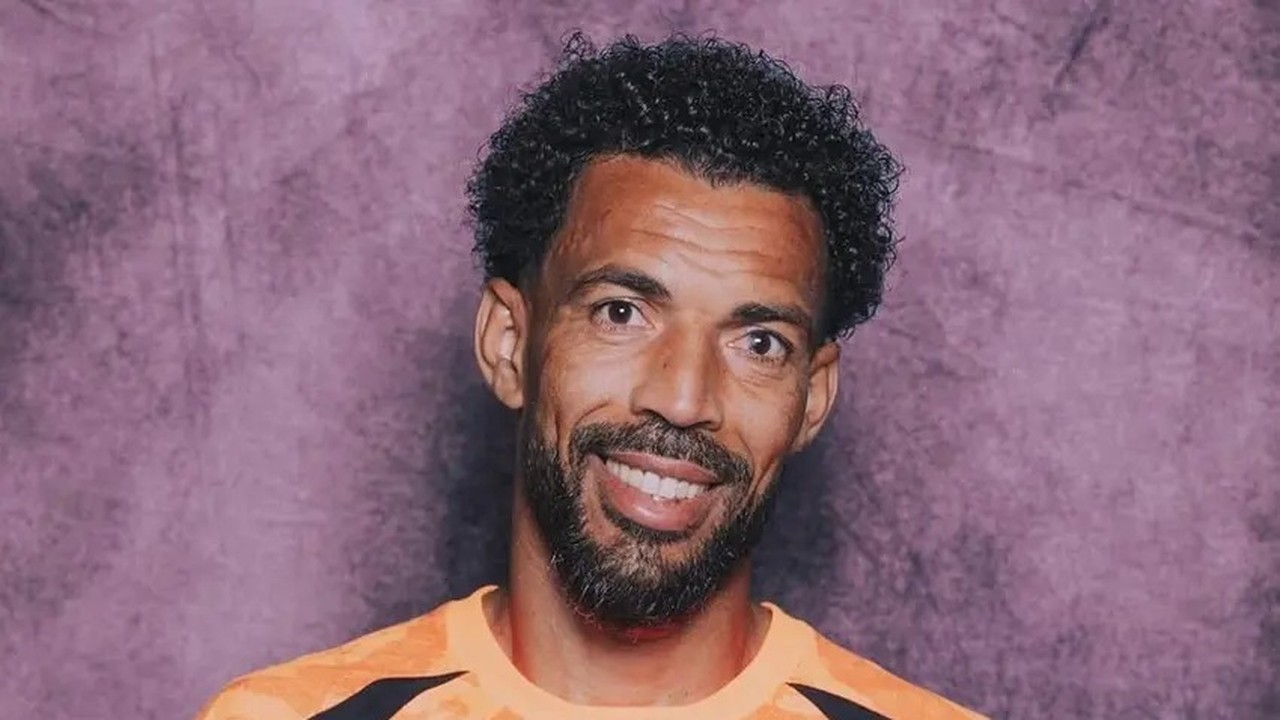 Retrato de Josimar Dias, o Vozinha, sorrindo com cabelo crespo, barba e camisa laranja.
